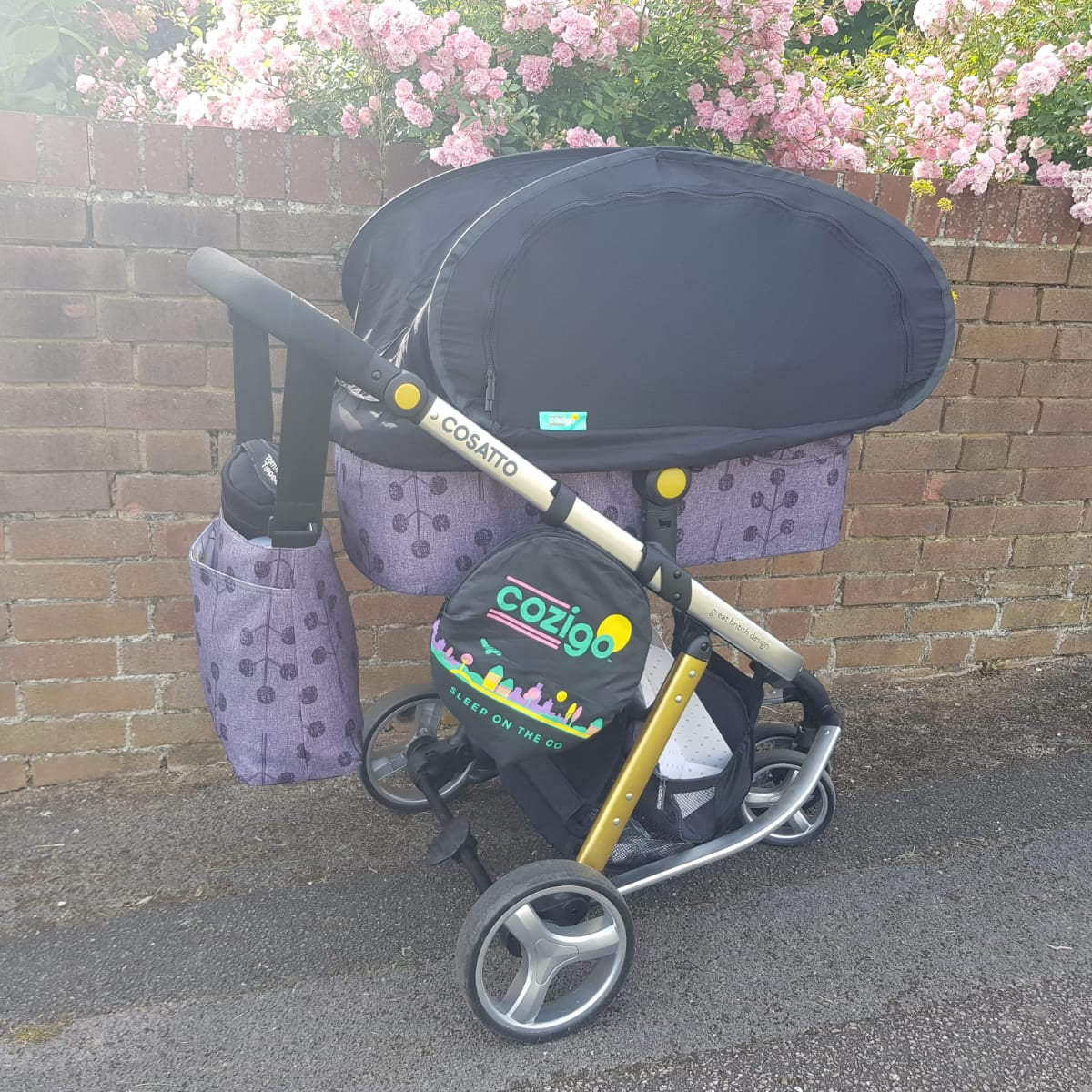 Cozy baby stroller with a black canopy against a brick wall with pink flowers.
