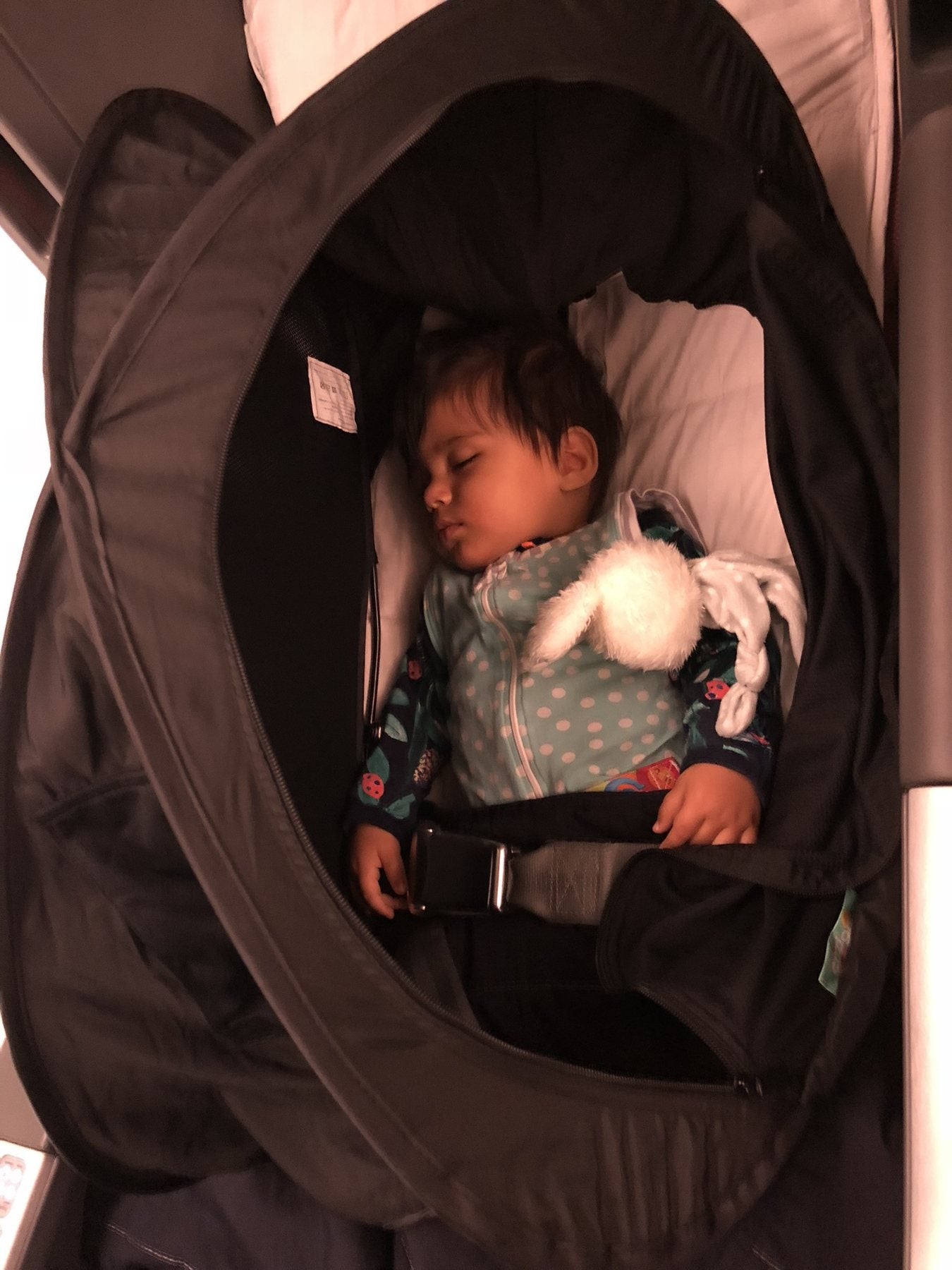 A baby asleep in an airline bassinet with CoziGo